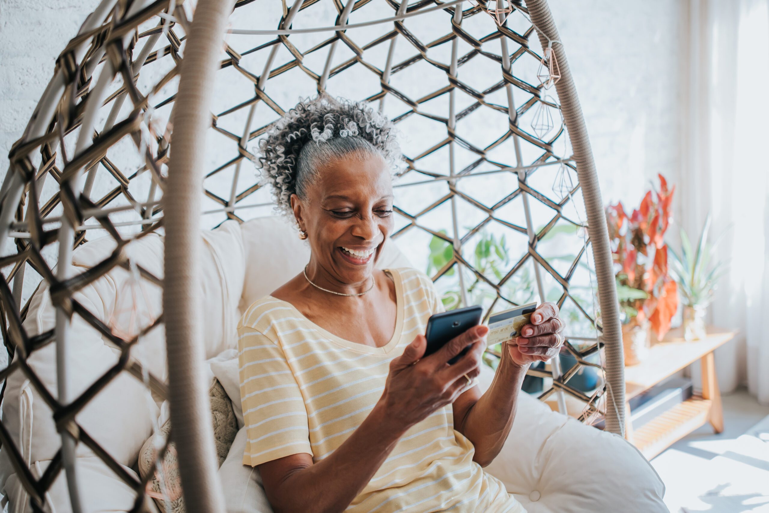 A senior woman using her credit card holding her cell phone in the living room of the house