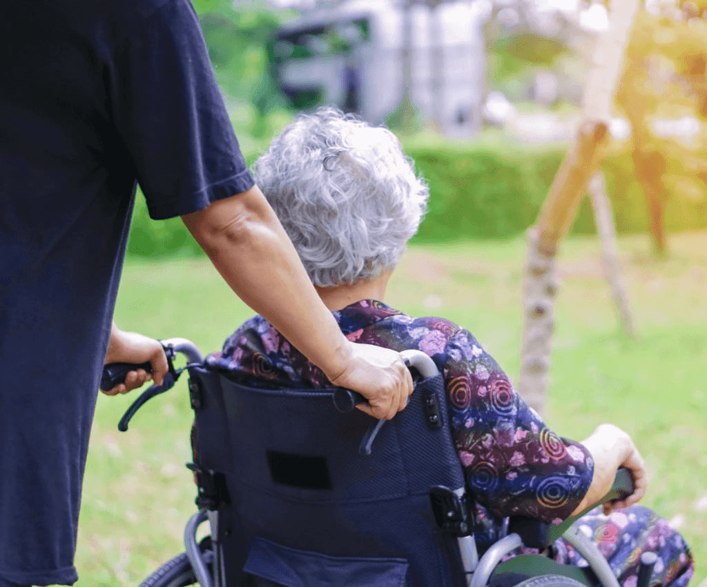 A carer pushing an elderly woman seated in a wheelchair