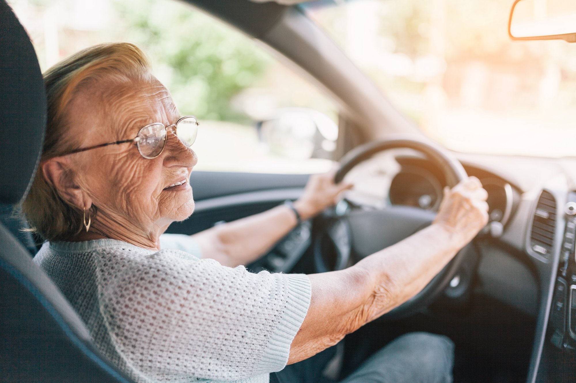 An elderly woman sitting in the driving seat of her car looking out the window.