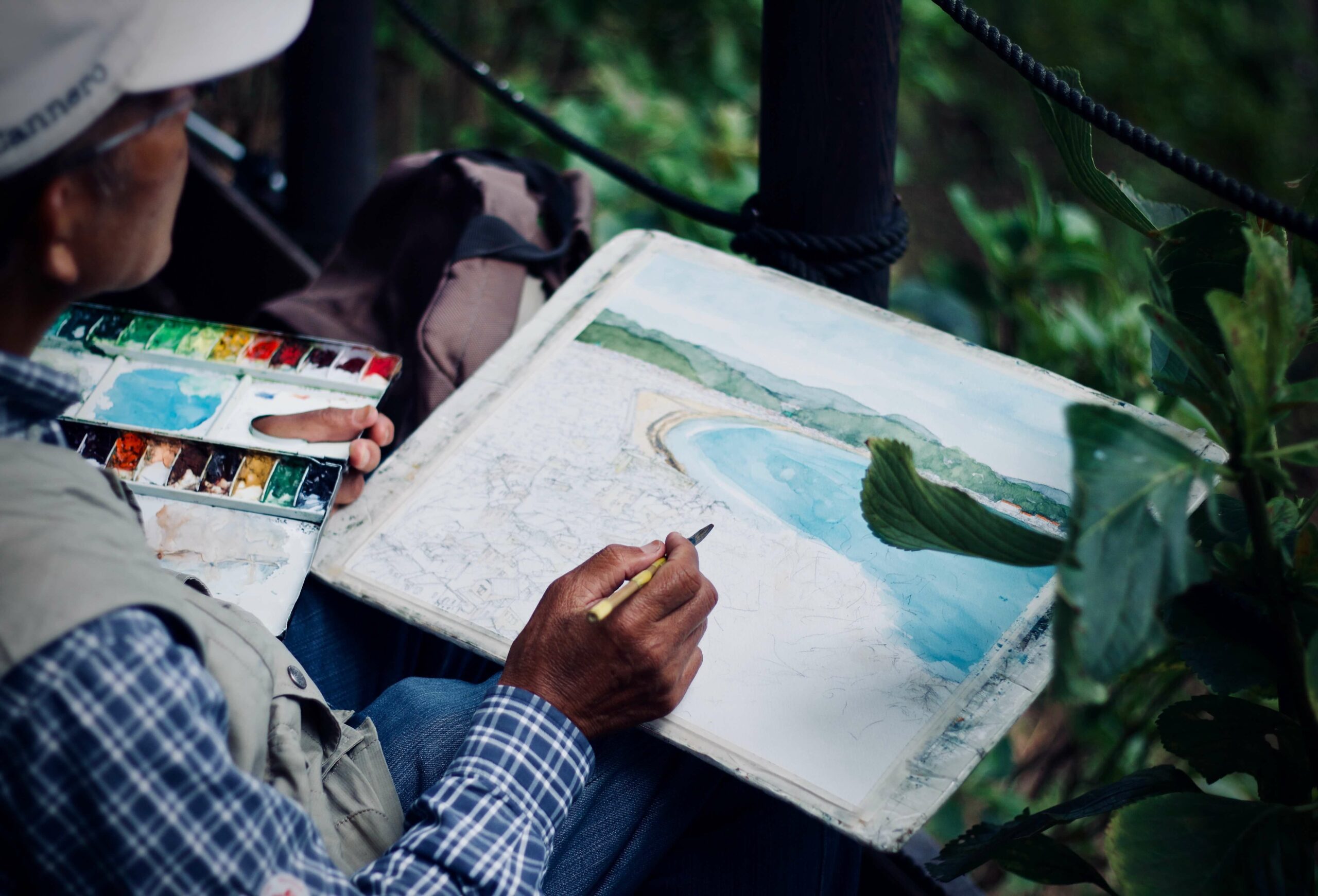 An Older Man Outside in a Wooded Scenic area Painting a Landscape in Watercolour Paints