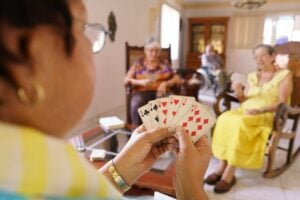 A close up of an older woman playing cards, alongside other older people chatting