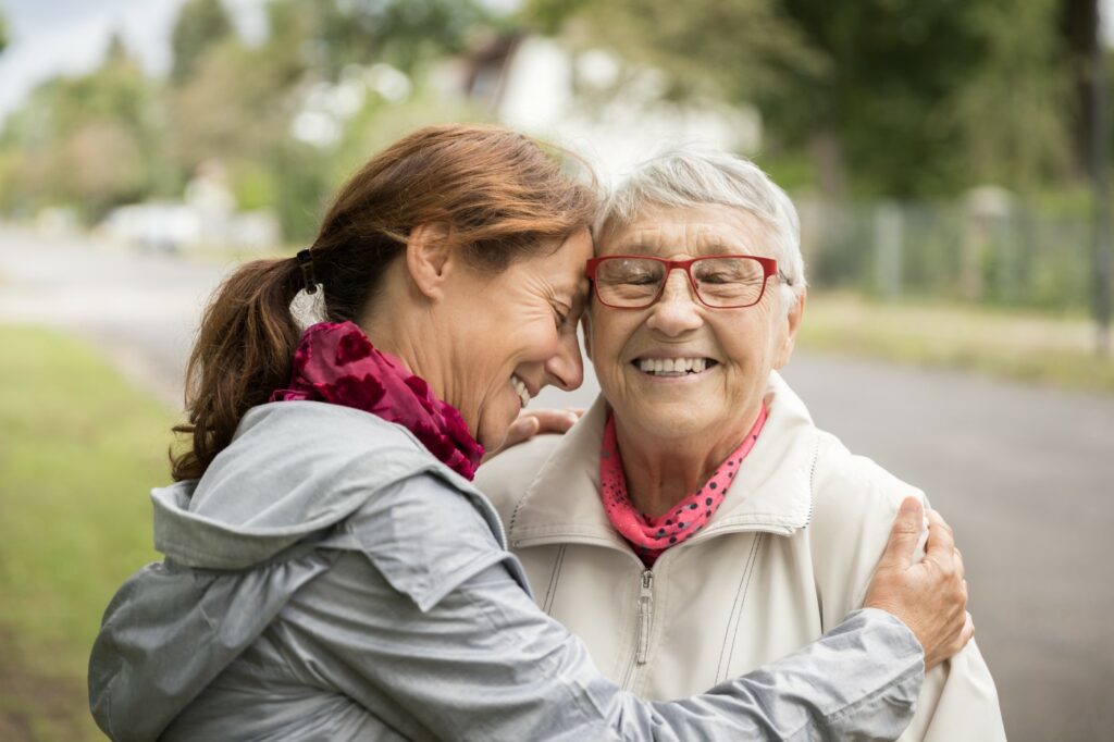 Middle aged daughter affectionately hugs her elderly mother during an autumn walk in the local park.