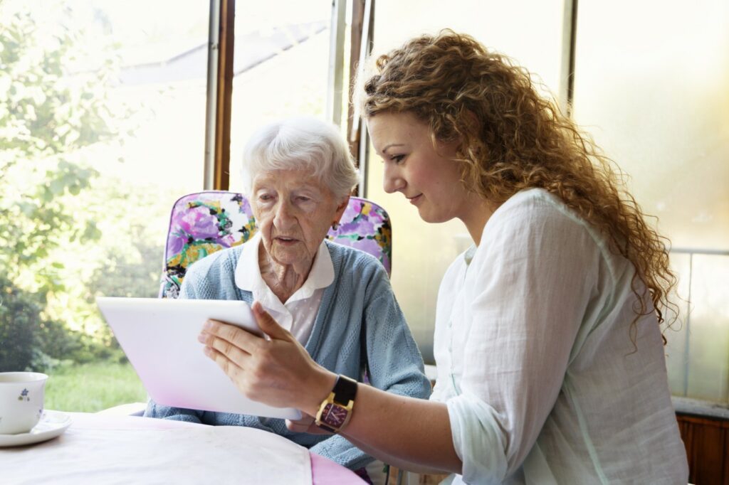 A young woman shows her elderly grandmother a video in an iPad whilst at home