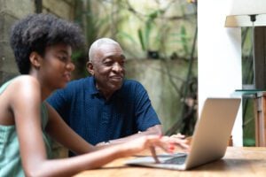 Granddaughter and grandfather using laptop at home