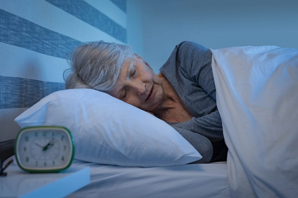 An older woman sleeps gently in bed alone.