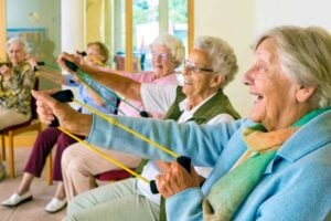 A class of older women Enjoying gentle arm stretch exercises while seated.