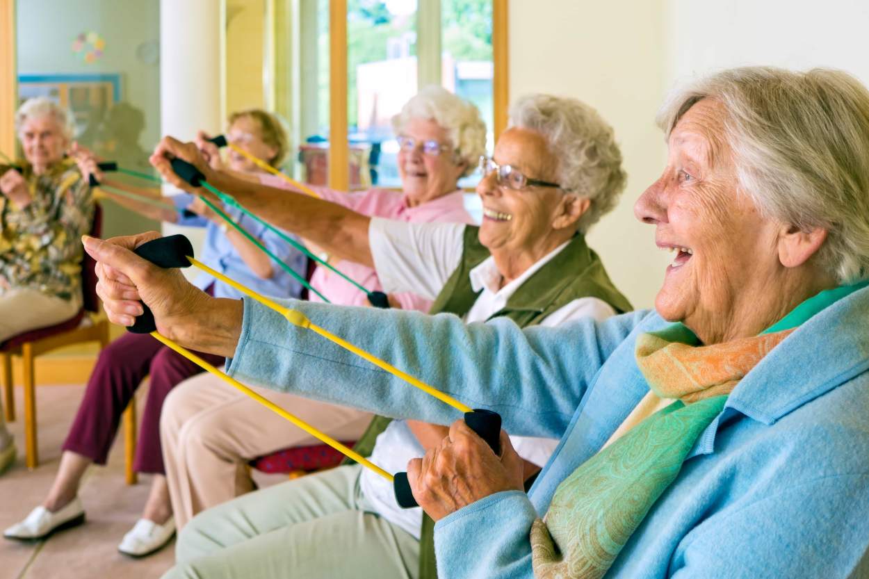 A class of older women Enjoying gentle arm stretch exercises while seated.