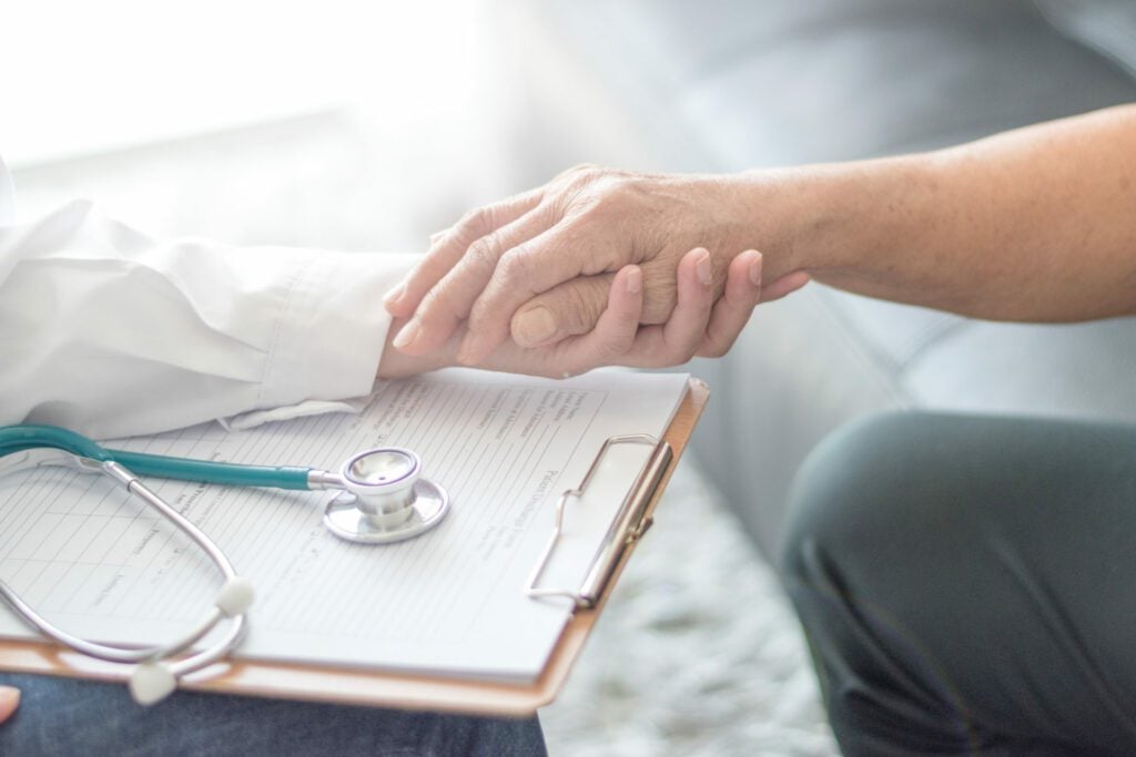 Healthcare professional holding palliative care patient's hand