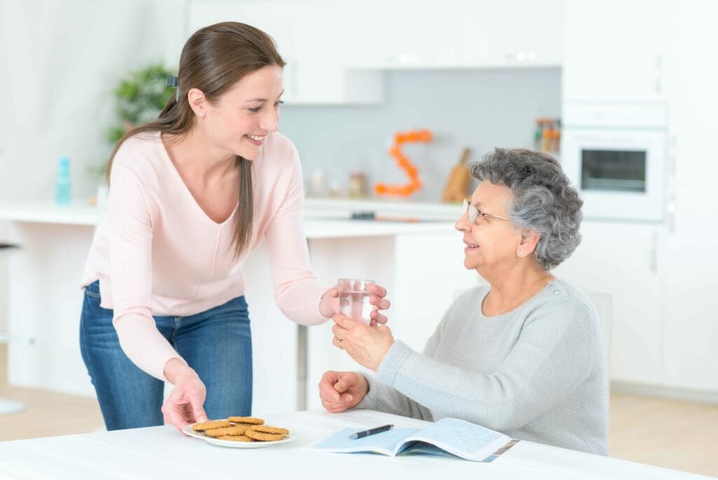 An elderly woman taking a glass of water from her carer