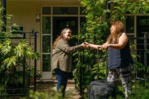 Elder live-in carer arrives with her suitcase and shakes hands with her customer outside the home on a sunny day.