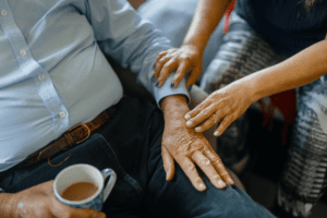 Elder live-in carer touches an elderly man's arm to provide comfort while he holds a cup of tea