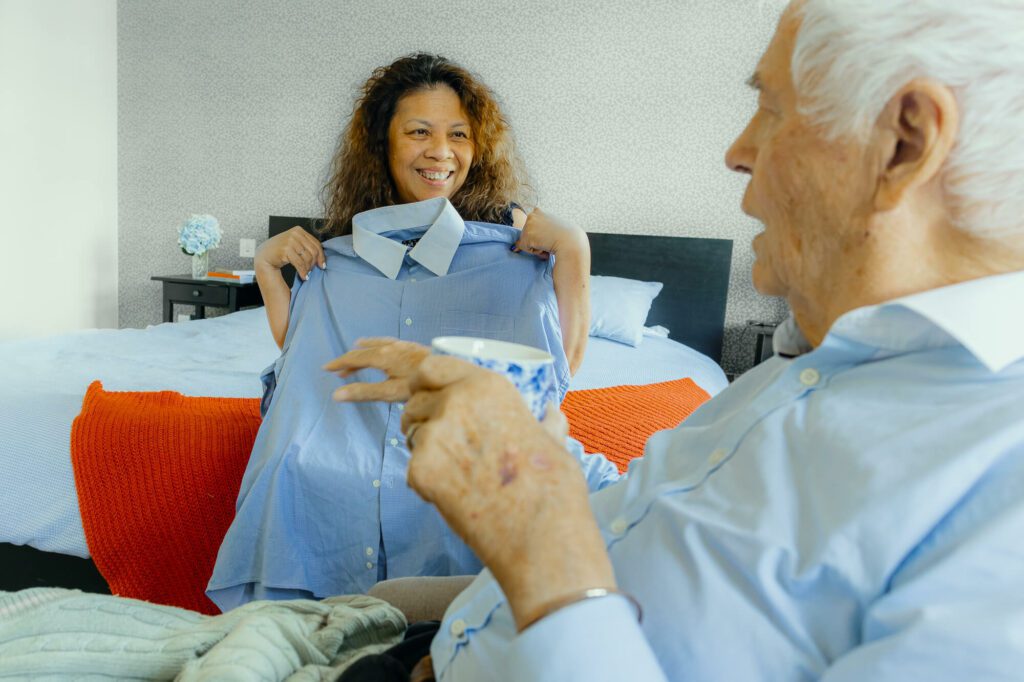 Elderly man is shown a shirt by his live-in carer, as an option to wear for the day ahead.