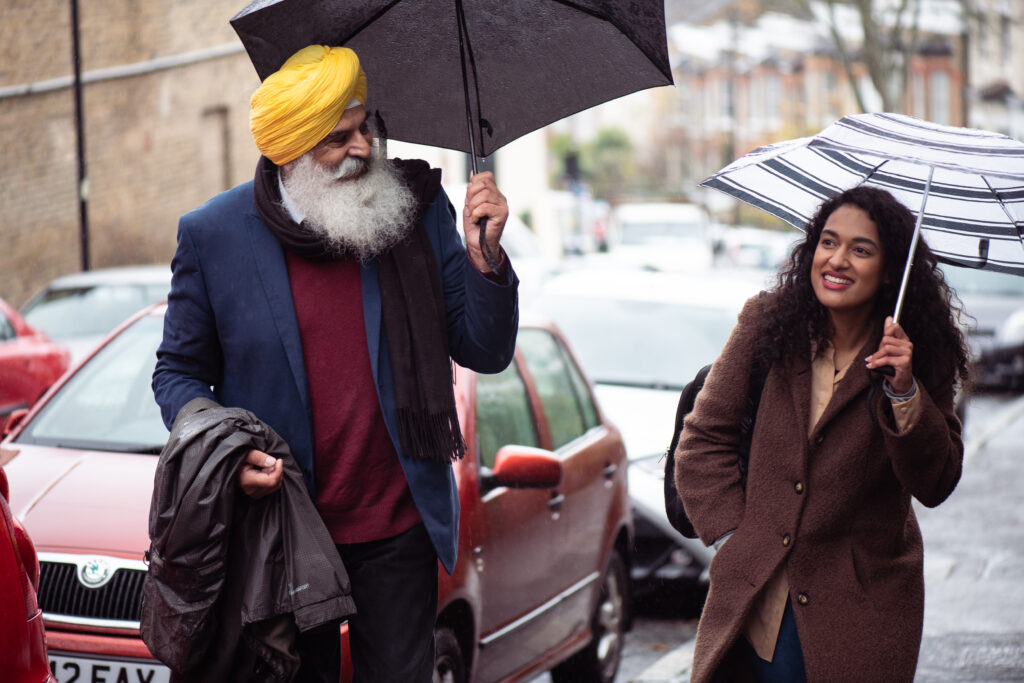 An elderly asian man taking a walk with his adult daughter in the street in the rain, both are using an umbrella.