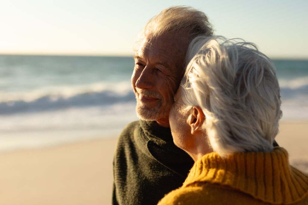 An older couple embrace on a beach on a windy winter day.