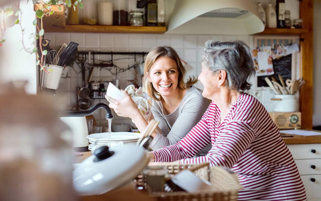 A young woman and her grandmother washing and drying dishes together at the kitchen sink