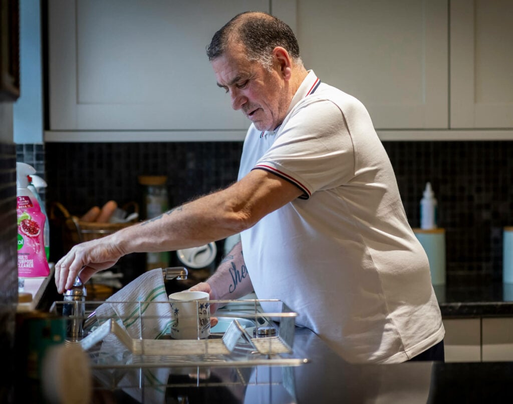 An older man does the dishes in his flat.