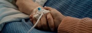 A close-up of two people holding hands, one person has a hospital IV line in their hand