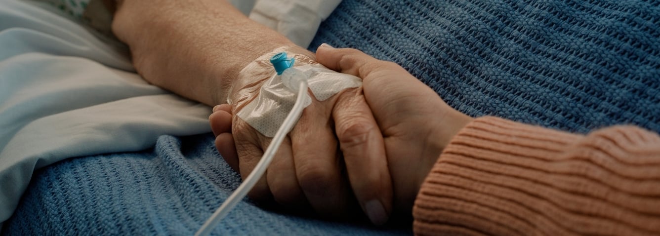 A close-up of two people holding hands, one person has a hospital IV line in their hand